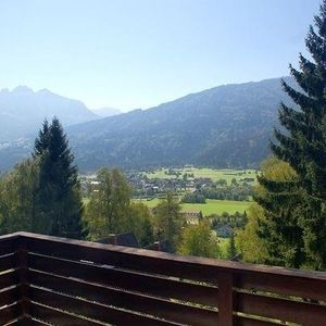Ein Balkongeländer aus Holz, im Hintergrund ist eine Landschaft zu sehen