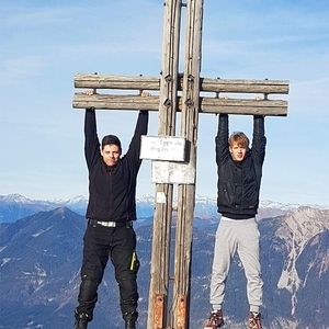 Zwei Männer hängen an einem Holzpfeiler vor einer Berglandschaft
