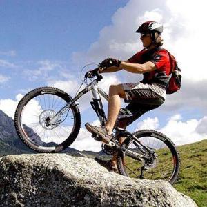 A man sits on a bicycle and stands on a hill